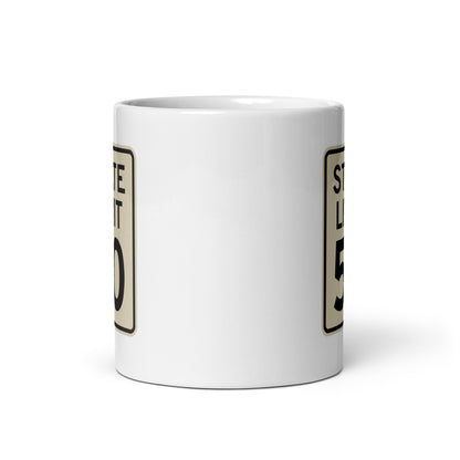 View of white ceramic mug with road sign graphic by State Limit Apparel to both sides.