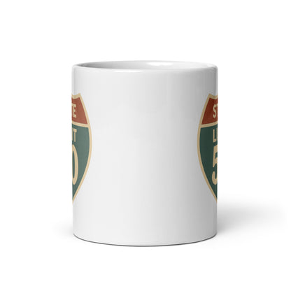View of white ceramic mug with road sign graphic by State Limit Apparel to both sides.